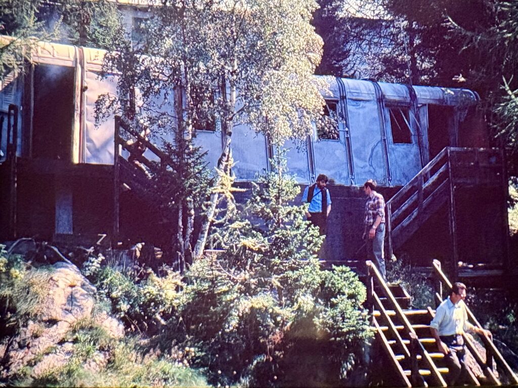 La struttura prefabbricata posta appena monte della casa Falck e che ospitava la cucina, la sala da pranzo e relax degli “Agipponi” completamente bruciata all’interno e la struttura metallica irrimediabilmente danneggiata. In foto mentre scende le scale ben riconoscibile il Geometra Lanzini, un pò il tutore dell’area. In alto a dx il nostro direttore lavori p.m. Bulf Luigi insieme al Geometra Tocalli, capo cantiere della Cariboni.